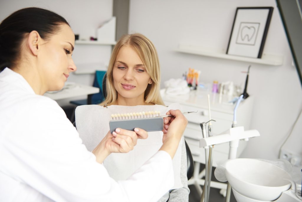 Female dentist and young woman choosing color teeth from palette